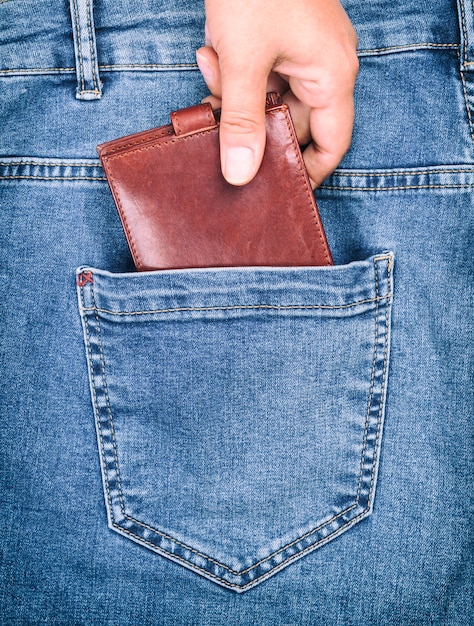 Brown leather purse lies in the back pocket of blue jeans