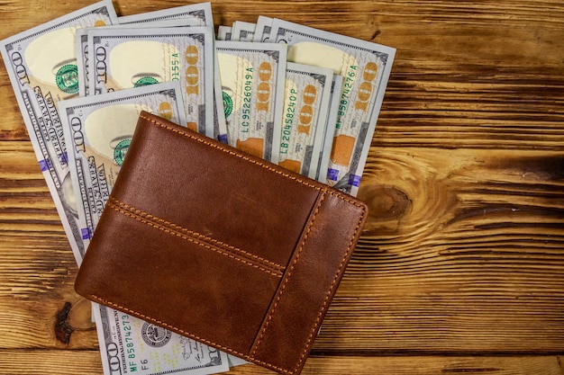 Brown leather wallet and american dollars on wooden table Top view