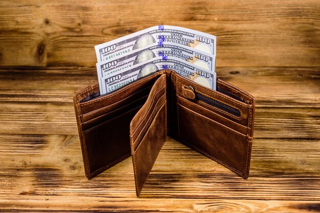 Brown leather wallet and one hundred dollar banknotes on the wooden background