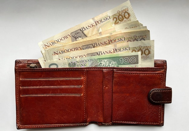 Brown leather wallet with 200 and 100 zloty bills in close-up on a white isolated background