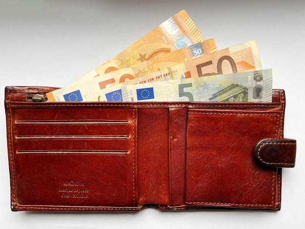 Brown leather wallet with 50 and 5 euro bills in close-up on a white isolated background