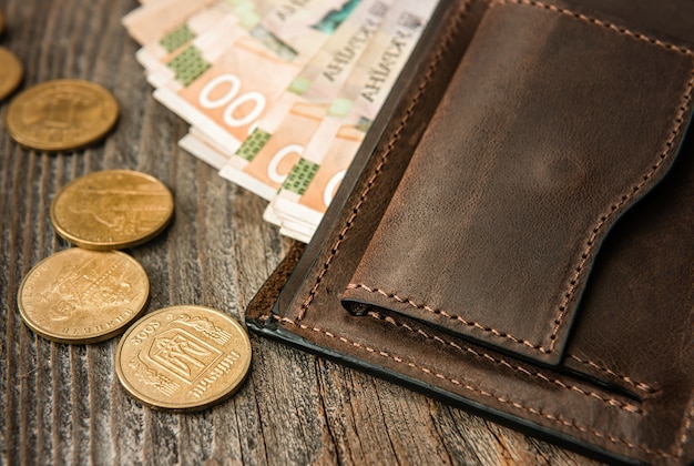 Brown leather wallet with banknotes and coins on old wooden surface. Close up.