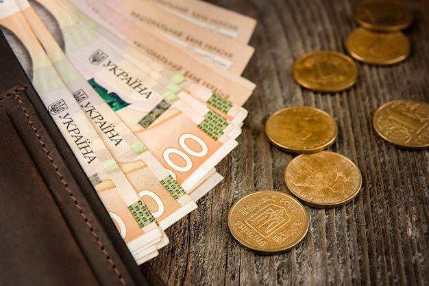 Brown leather wallet with banknotes and coins on old wooden surface