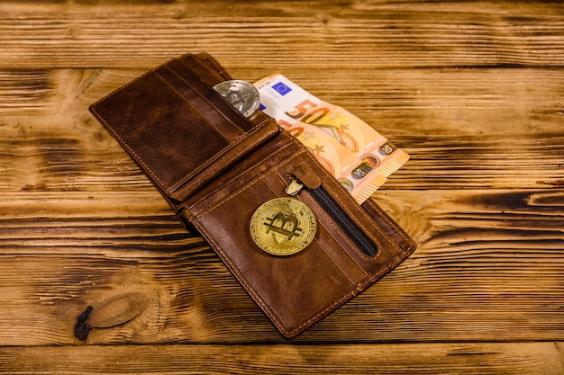 Brown leather wallet with fifty euro banknotes and bitcoins on the wooden background