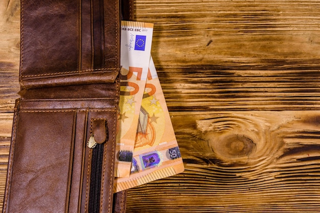 Brown leather wallet with fifty euro banknotes on the wooden background Top view