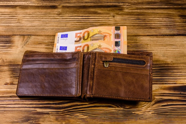 Brown leather wallet with fifty euro banknotes on the wooden background