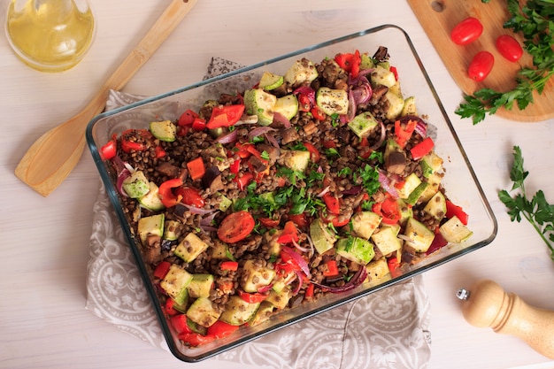 Lenticchie marroni cotte in forno con pomodori, zucchine e altre verdure in una teglia di vetro