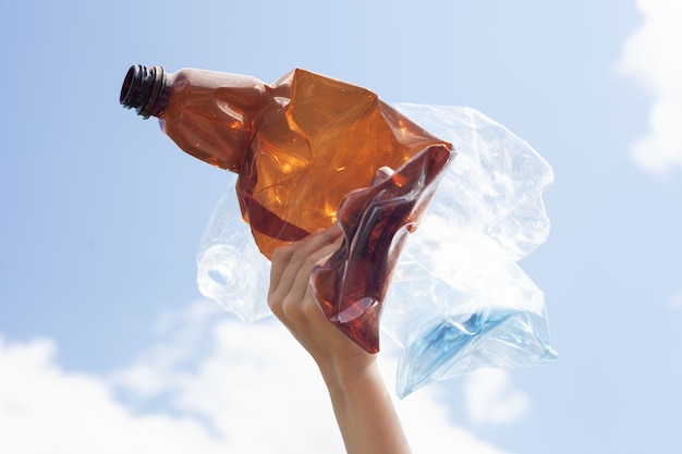 Brown and light plastic bottles are crushed and are in the child's hand against the background of a blue sky with blocks.