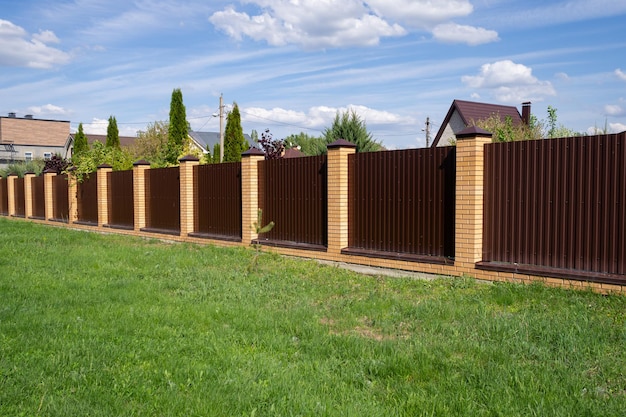 A brown metal fence with brick posts against a sky. A high wall encloses the private area. Security concept