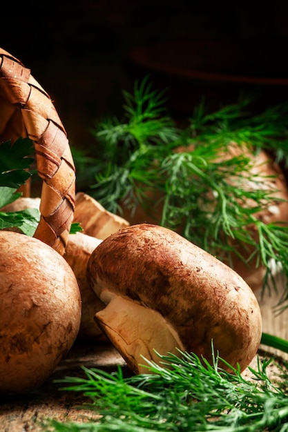 Brown mushrooms parsley and dill a wicker basket on an old wooden background selective focus