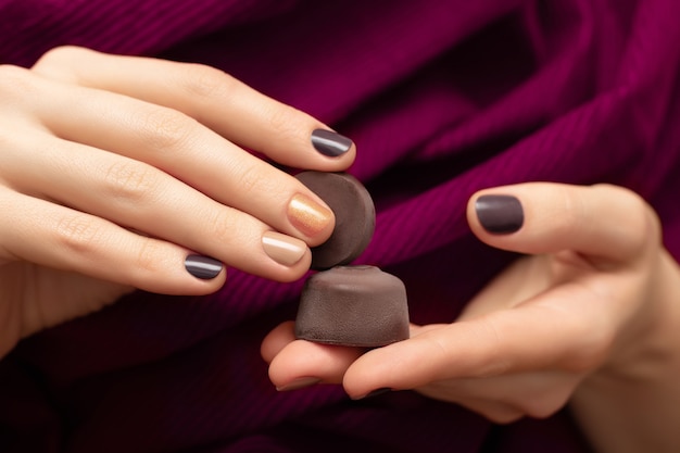 Brown nail design. Female hands holding chocolate candies.