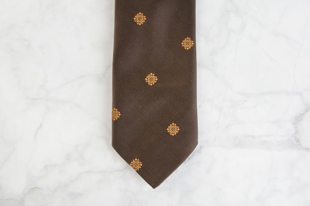 Brown neck tie with geometric pattern on marble background. Copy space for text.