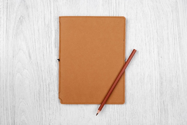 Brown notebook and a pencil on white wooden table top view