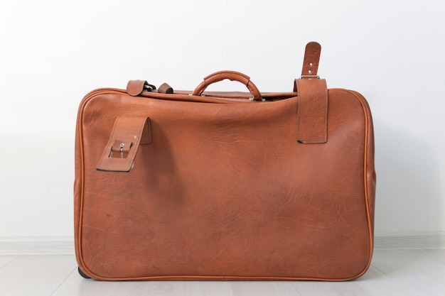 A brown old leathery closed suitcase in retro style is located near the white wall