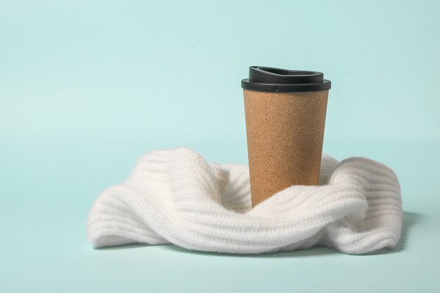 Brown paper coffee Cup wrapped in a scarf on a blue