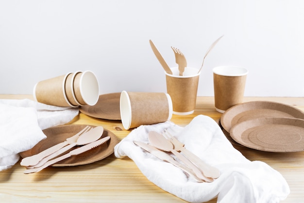 Photo brown paper cups, plates, wooden cutlery, linen napkins on wooden background