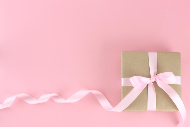 파스텔 핑크 배경에 분홍색 새틴 곱슬 리본 활이 있는 갈색 종이 선물 상자 플랫 레이 어머니 날 아버지 날 발렌타인 데이 생일 개념 복사 공간