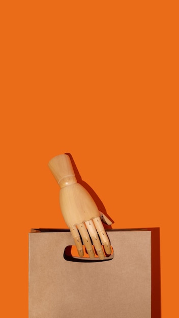 Brown paper package with wooden hand on orange background\
mockup