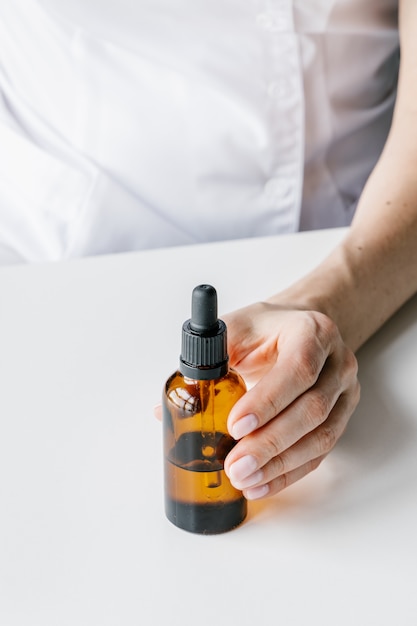 Brown plastic bottle for liquid cosmetics in woman's hand. Cosmetologist holding spin care product.