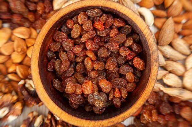 Brown raisins in a wooden cedar plate on the background a scattering of various nuts.