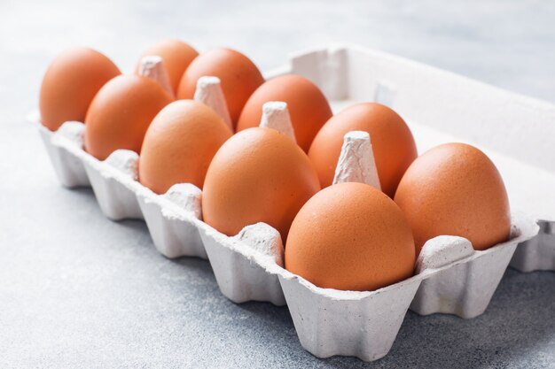 Il pollo crudo di brown eggs in imballaggio della fabbrica su fondo grigio.