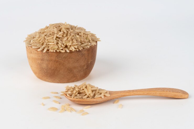 Photo brown rice in a wooden bowl and spoon overflowing out and scattered on the floor.