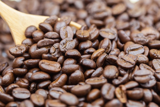 Brown roasted coffee beans texture with wooden spoon background.