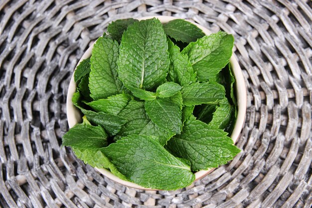 Brown round bowl of fresh mint leaves on a wooden stand