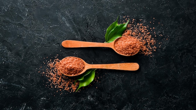 Brown sea salt in a spoon. On a black stone background. Spa treatments. Top view. Free copy space.