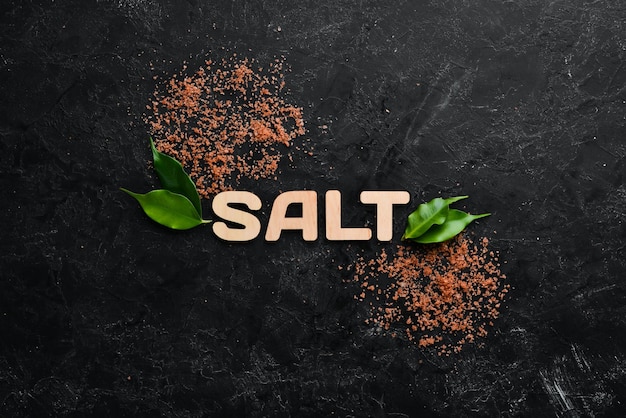 검은 돌 배경에 SALT라는 글자가 있는 갈색 바다 소금 스파 트리트먼트 상위 뷰 무료 복사 공간