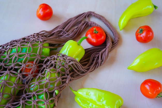 Brown string bag knitted in macrame technique from a knitted cord with green bell pepper and tomatoes on a wooden background Flat lay top view Zero waste and plastic free concept A place for text