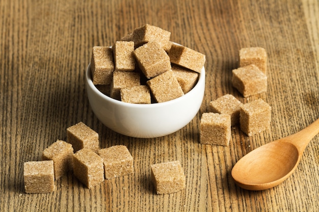 Brown sugar cubes in a white bowl and on a wooden table