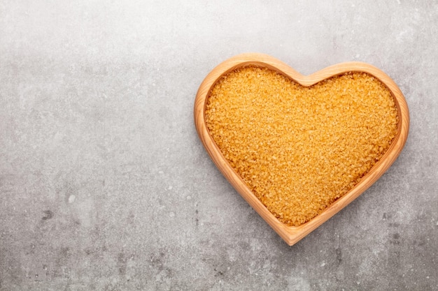 Zucchero di canna a forma di ciotola di legno del cuore su sfondo pastello