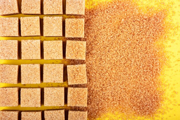 Brown sugar. Mix of cubes and sand on yellow background