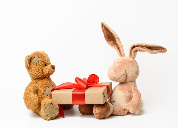 Brown teddy bear and rabbit holding a box with a gift on white