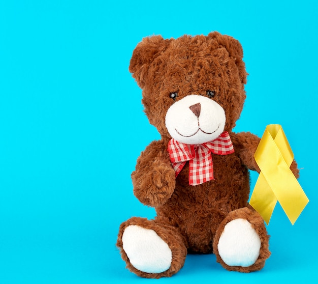 Brown teddy bear sits and holds in his paw a yellow silk ribbon 