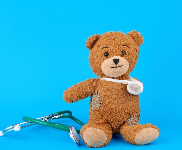 Brown teddy bear with a bandaged paw sitting on a blue background