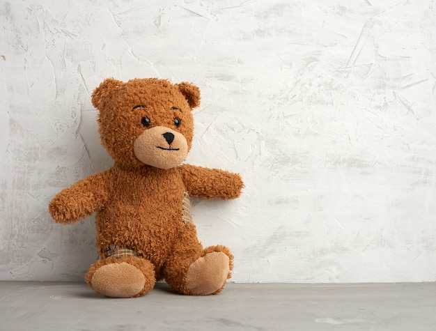 Brown teddy bear with patches sits on a white background