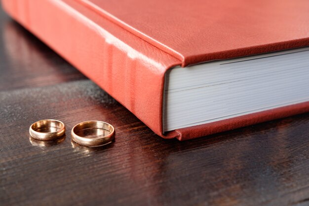 Brown wedding album with two wedding rings lie on brown wooden table