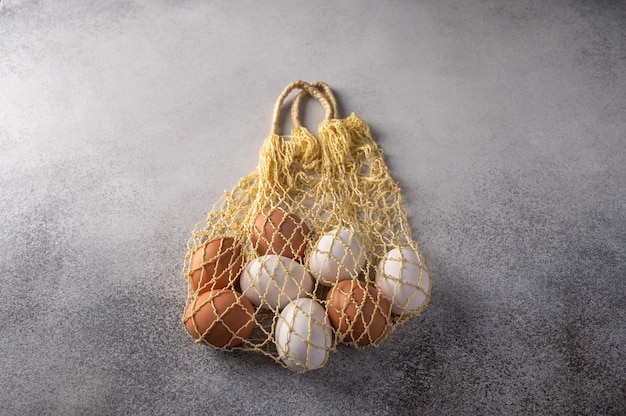 Brown and white chicken eggs in string bag on a light textured background.