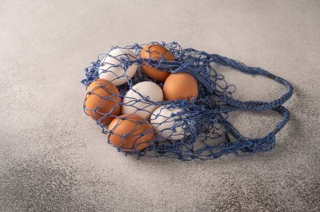 Brown and white chicken eggs in string bag on a light textured background.