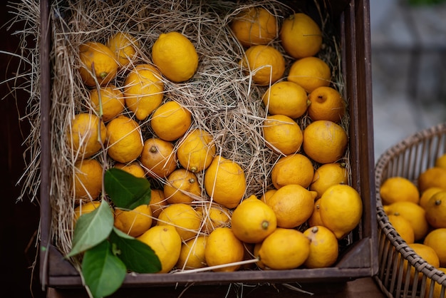 Foto in una scatola di legno marrone, nella paglia ci sono limoni giallo arancio con rametti verdi. decorazioni fresche e vivaci per la decorazione della fiera del festival. succhi di frutta naturali. copia spazio