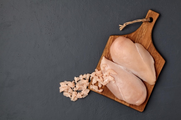 Foto tagliere in legno marrone con filetto di petto di pollo tritato su un tavolo di cemento scuro vista dall'alto con spazio per la copia posa piatta