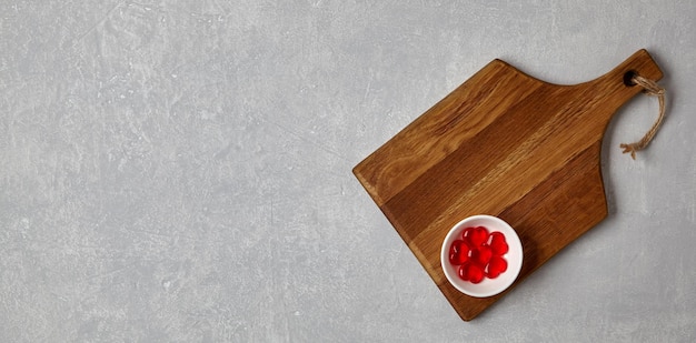 Brown wooden cutting board with red caramel hearts in a bowl on a gray concrete table Banner for demonstrating the layout of romantic dishes Top view with copy space flat lay