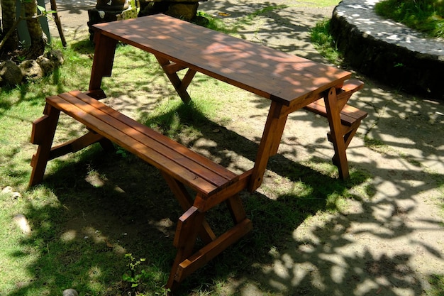 Brown wooden table and chairs in a shady tropical garden. the\
yard is overgrown with green grass