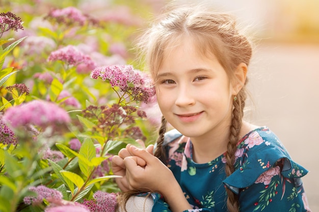 갈색 머리 의 소녀 가 덤불 에 있는 분홍색 꽃 근처 에 포즈 를 취 하고 있다