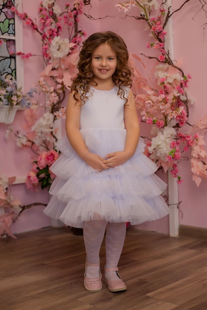 a brownhaired girl in a white dress stands against a background of flowers in the studio