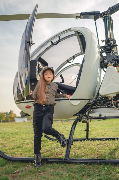 Brownhaired tween girl in visor cap standing near helicopter