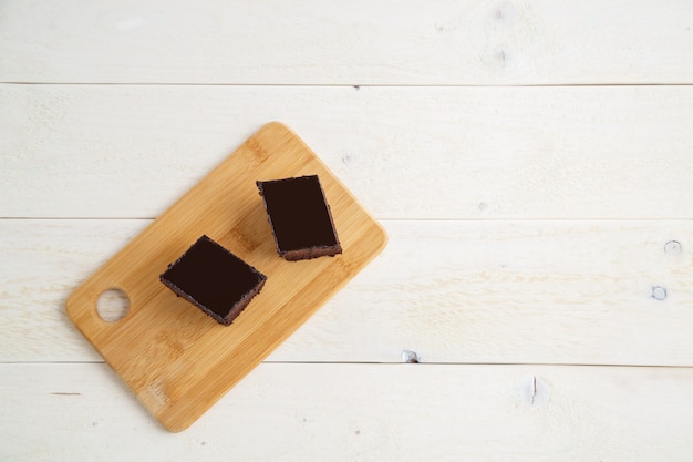 Brownie cake on a bamboo tray on a white wooden background with space for text