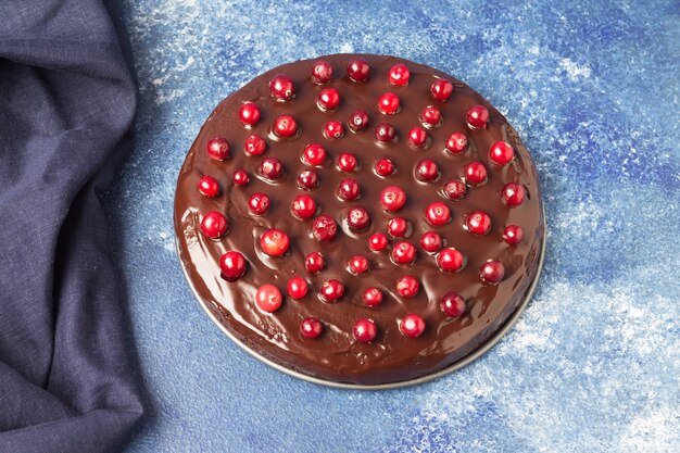 Foto torta brownie con glassa al cioccolato, decorata con mirtilli rossi, su sfondo blu. senza glutine. mangiare sano